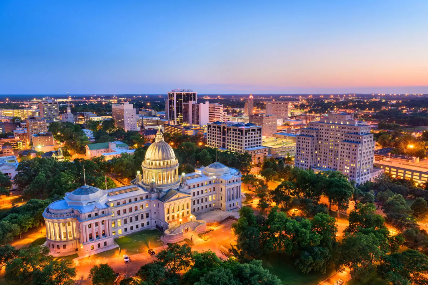 Jackson, Mississippi skyline at dusk. The Mississippi State Capitol, a domed building, is prominently featured in the center of the image.