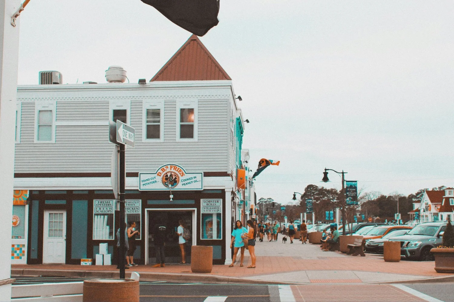 A bustling street scene in Rehoboth Beach, Delaware, with colorful buildings, pedestrians, and parked cars