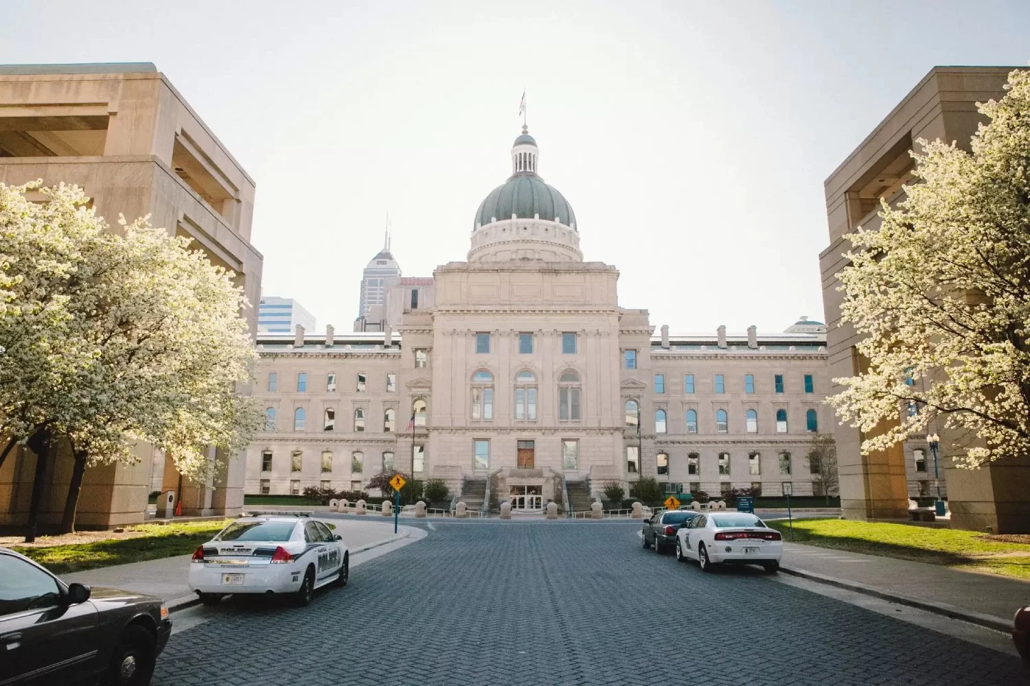 Front view of the Indiana State Capitol building in Indianapolis, with trees and parked cars