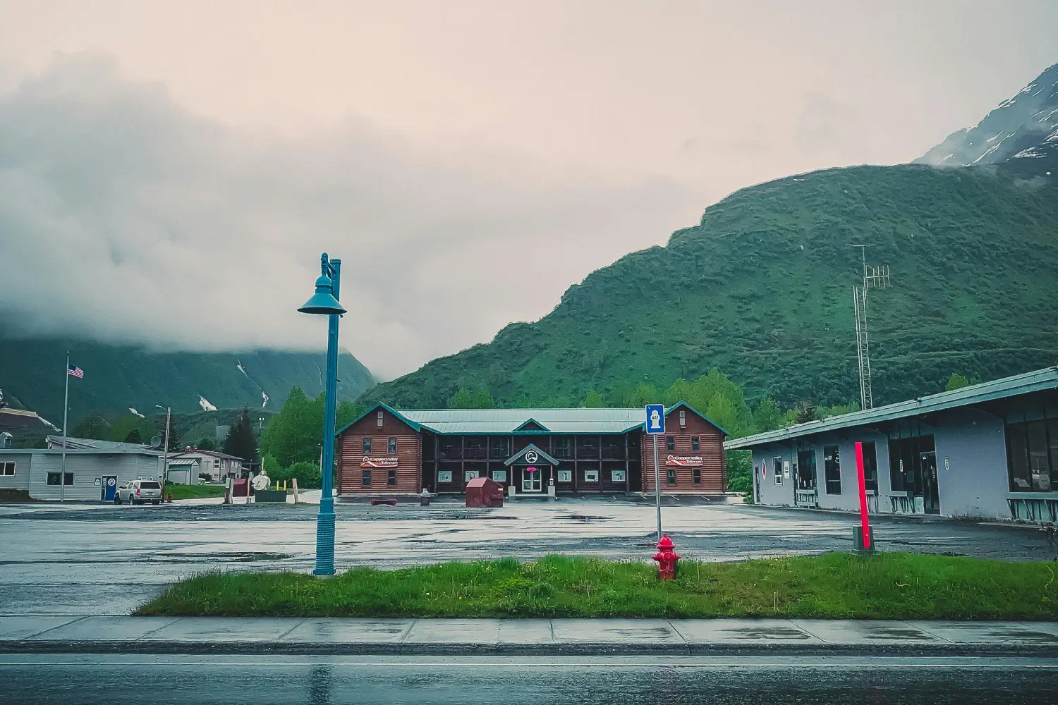 Alaska town with log-cabin hotel, empty parking lot, and mountains in the background.