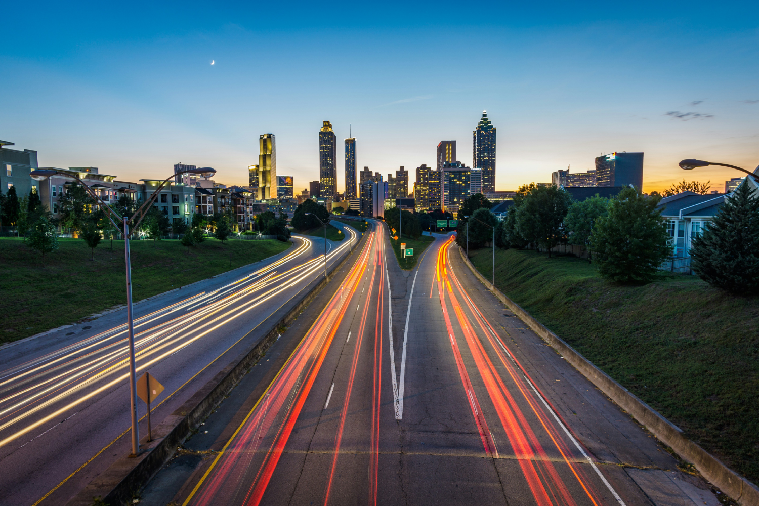 Long exposure of Atlanta highway at dusk with light trails and city skyline.