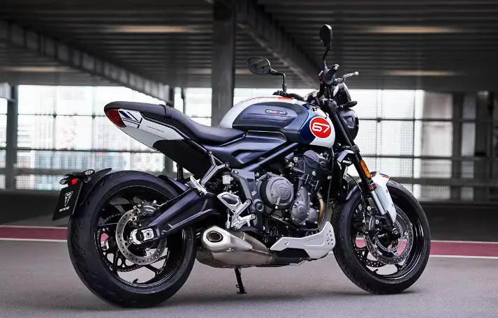 A white, blue, and red Triumph Trident 660 motorcycle with sporty styling, upright seating, and modern LED headlights, parked on a paved road