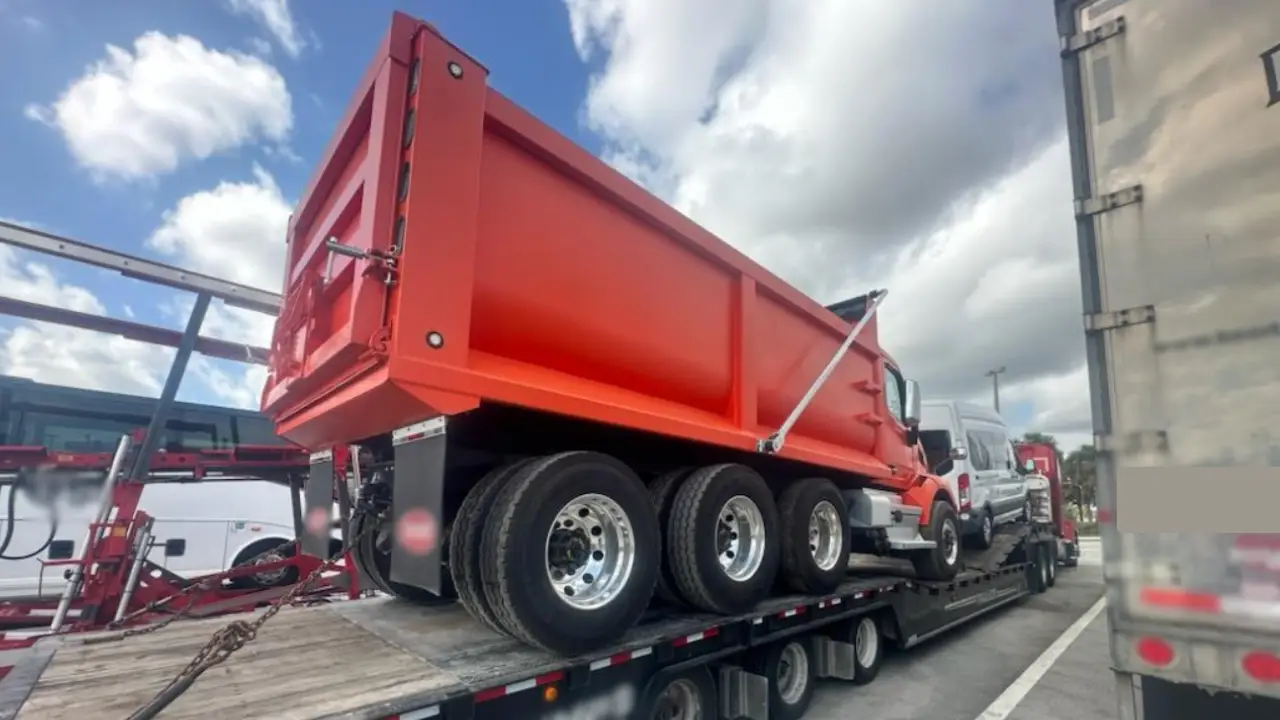 Red dump truck being transported on a flatbed trailer with other vehicles
