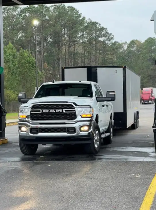 RAM truck with enclosed auto transport trailer refueling at gas station during cross-country vehicle shipping from North Carolina to Colorado.