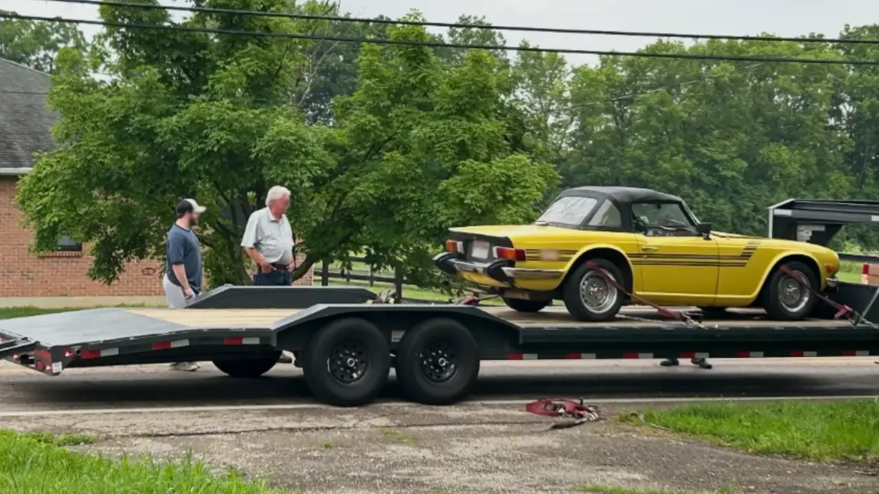 Classic yellow sports car loaded onto trailer by two men showing professional vehicle shipping