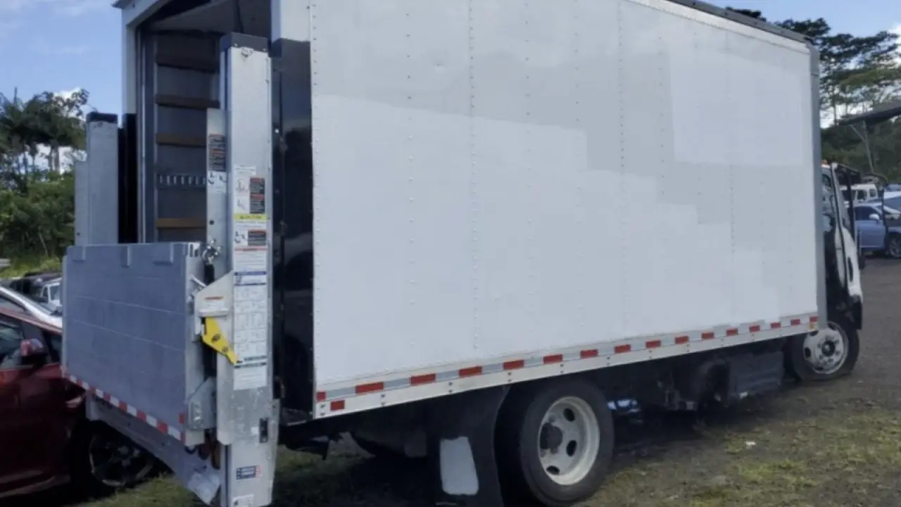 A white AutoStar Transport Express Izuzu box truck with its liftgate lowered, ready for loading.