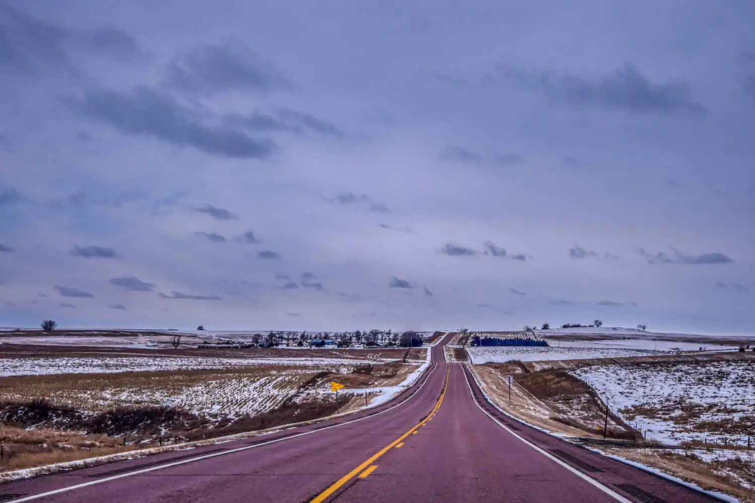 Empty road through snowy South Dakota landscape with rolling hills and cloudy blue sky