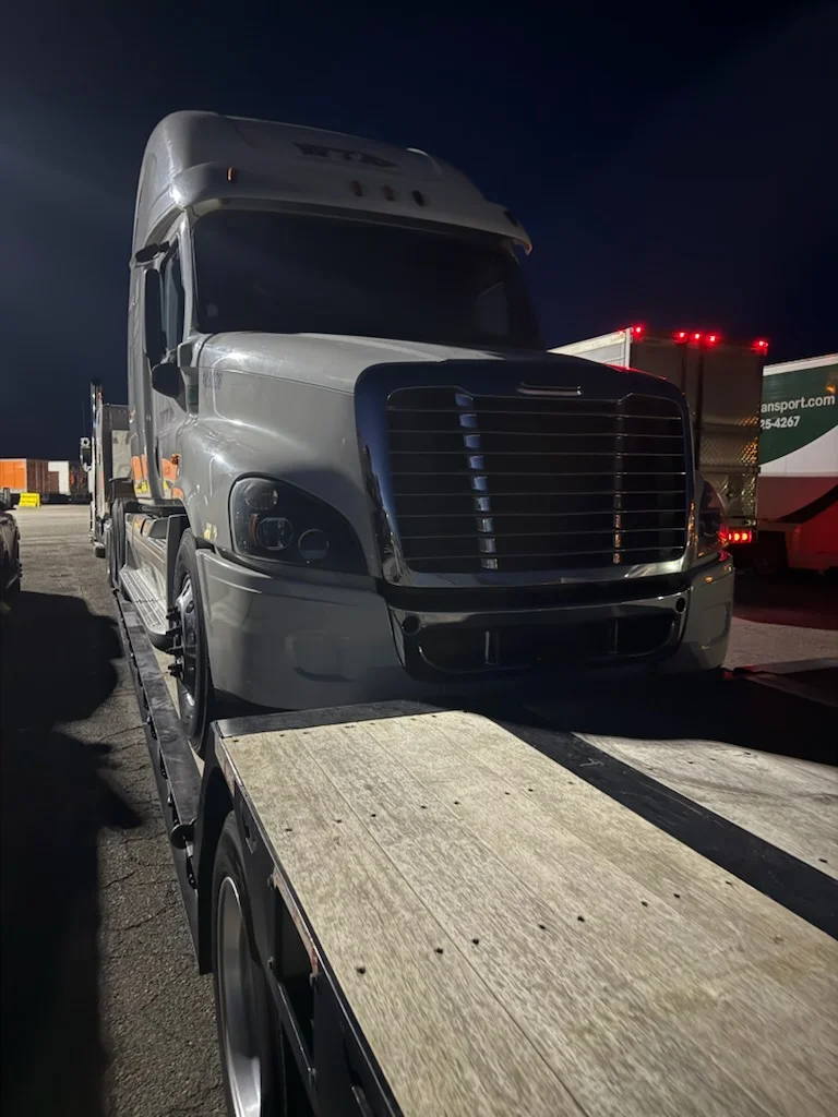Freightliner semi-truck on AutoStar Transport Express flatbed for safe nighttime heavy vehicle shipping