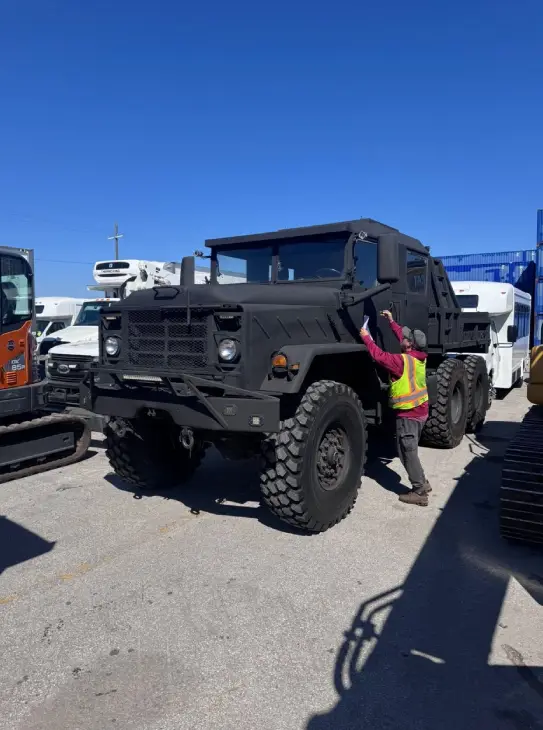 Heavy-duty military transport truck (M939) being inspected before shipment by AutoStar Transport Express personnel.