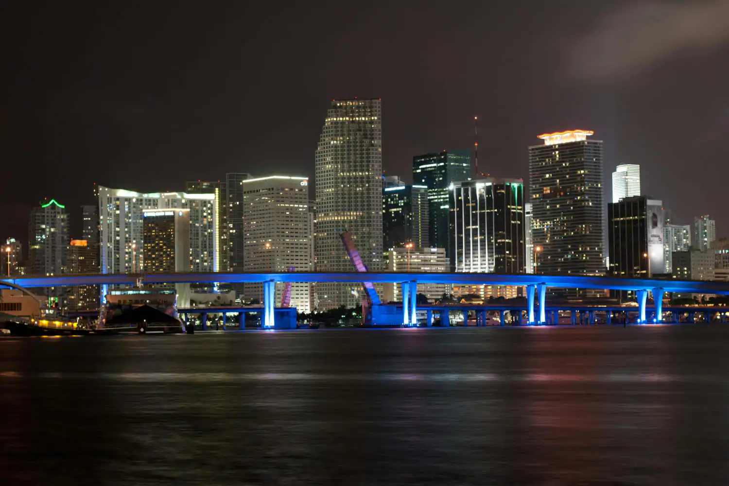 A vibrant night view of the Miami, Florida skyline, illuminated with colorful lights.